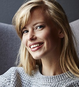 Woman in gray sweater sitting on touch and grinning