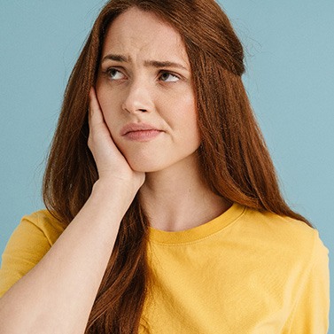 Woman in yellow shirt holding hand to sore jaw