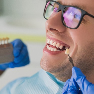 Dentist holding sample tooth to gap in man’s grin