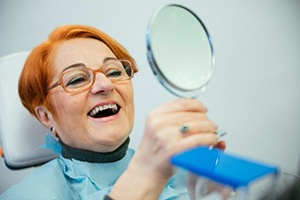 A senior woman admiring her dentures in a hand mirror