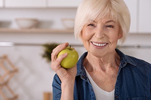 Senior woman holding apple and smiling with dental implants in Lakewood, CO
