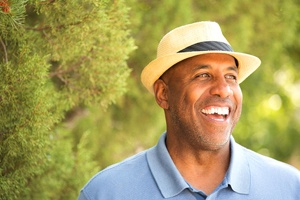 older man in blue polo and fedora smiling among trees