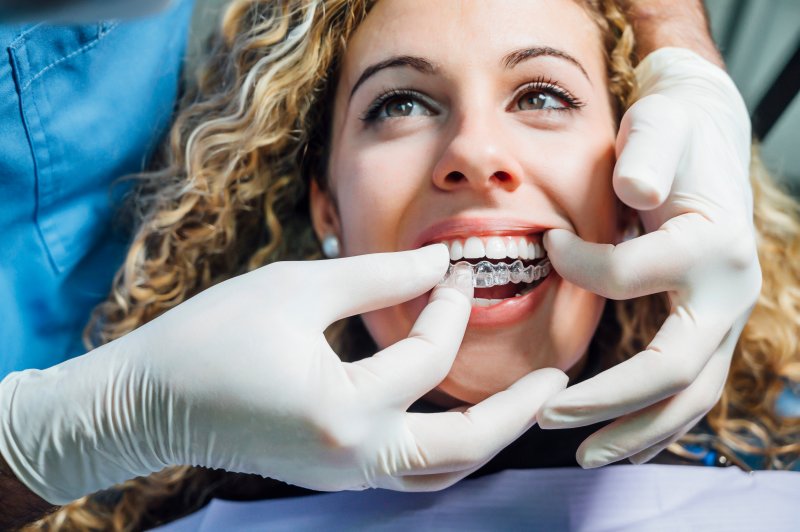 Dentist putting Invisalign aligner on patient’s teeth 