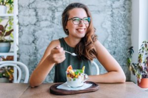 a woman smiling and eating foods that help her veneers’ lifespan