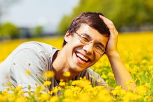 Young man with glasses smiling in a field of yellow flowers. 