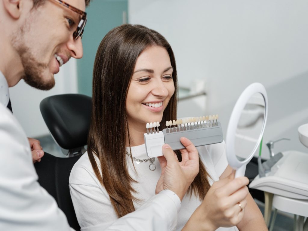 Cosmetic dentist showing smiling woman different shades of veneers