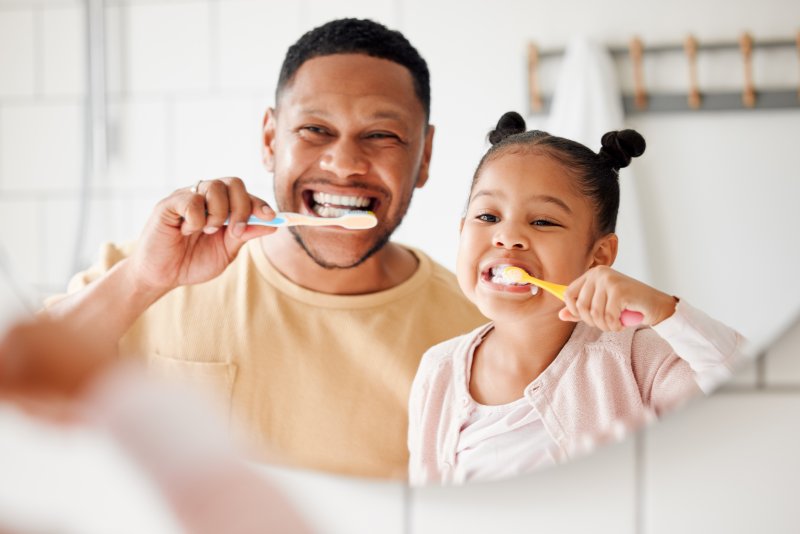 A father and daughter brushing their teeth in the mirror for good oral health in the new year