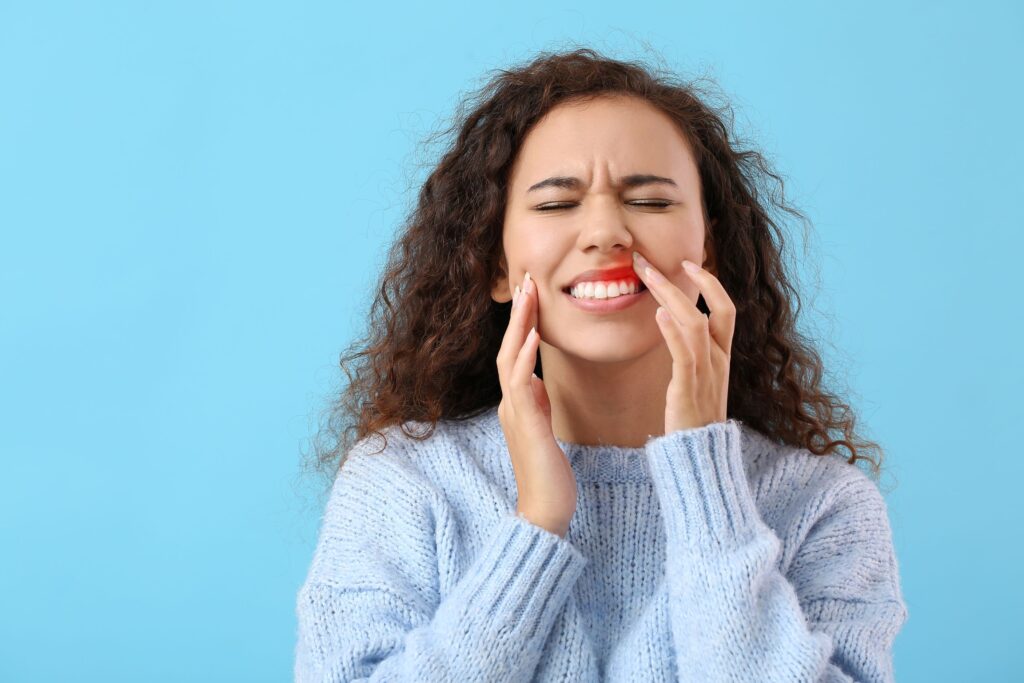 Woman in blue sweater touching red swollen gums with finger