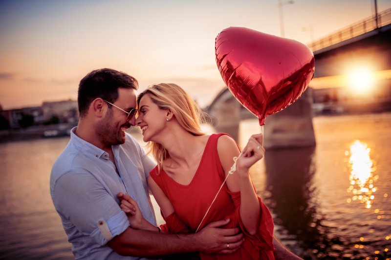 a couple smiling while holding red heart balloon